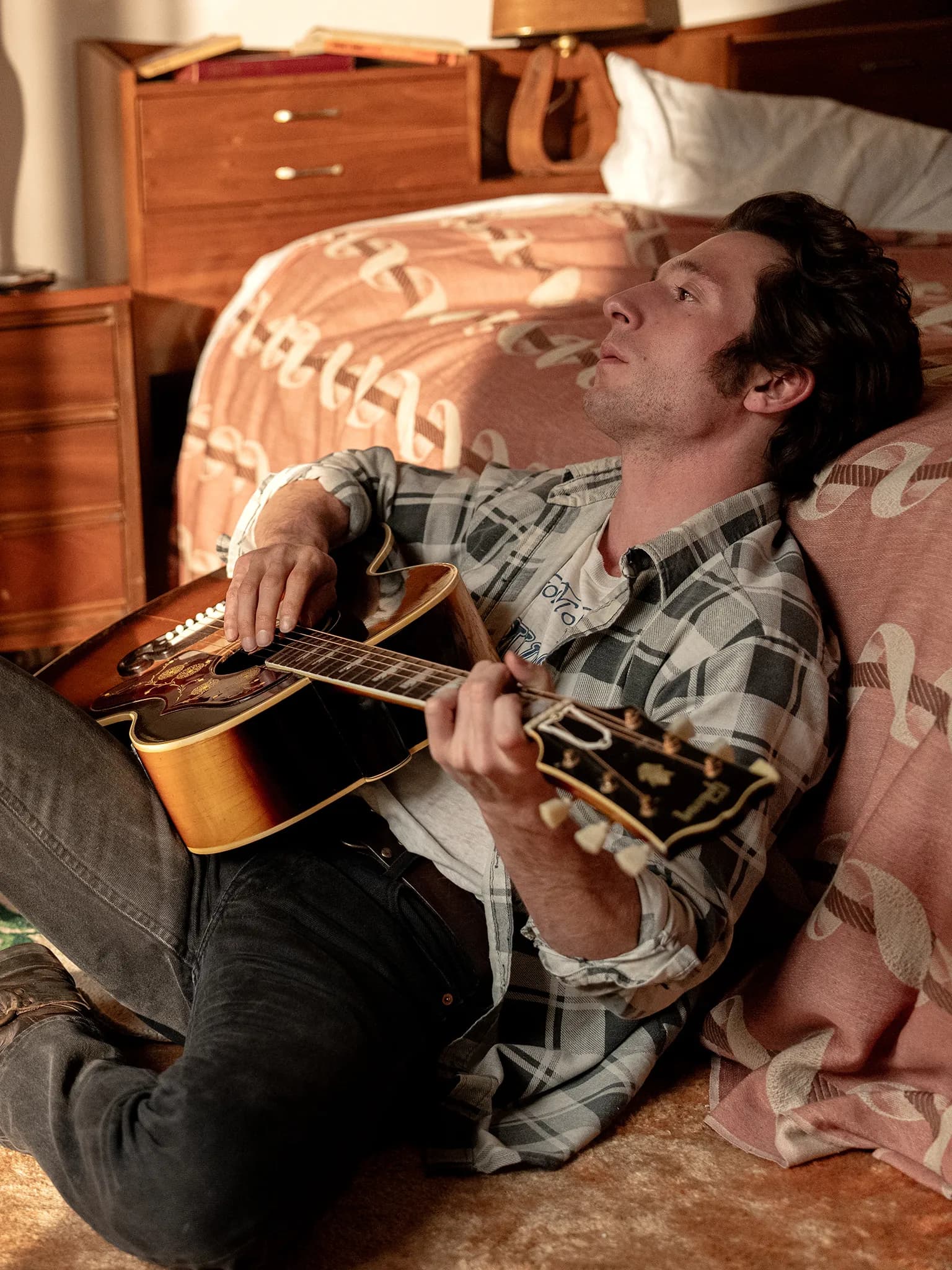 Actor Jeremy Allen White as Bruce Springsteen, leans against his bed and holds his guitar in a still from "Deliver Me From Nowhere." 