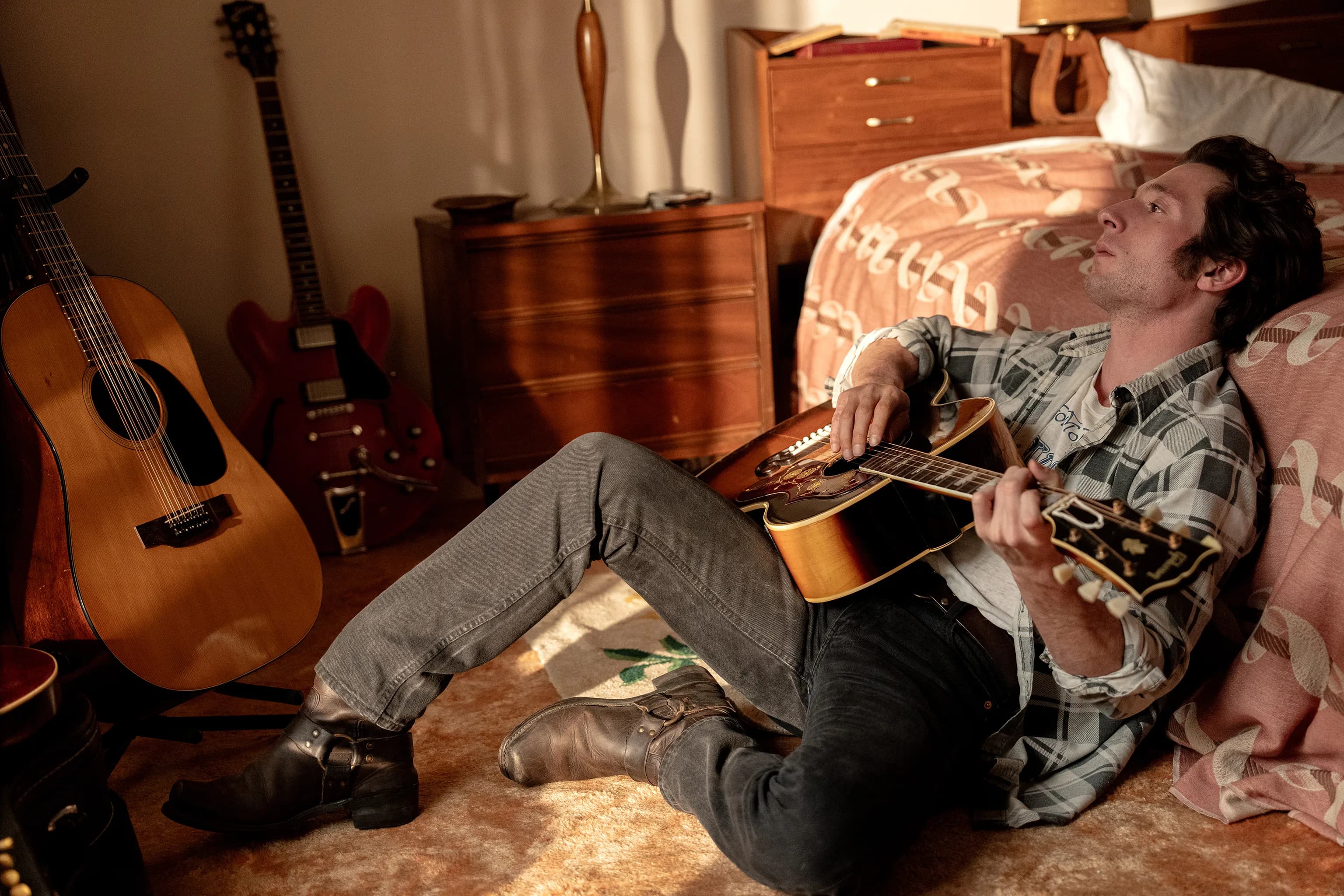 Actor Jeremy Allen White as Bruce Springsteen, leans against his bed and holds his guitar in a still from "Deliver Me From Nowhere." 