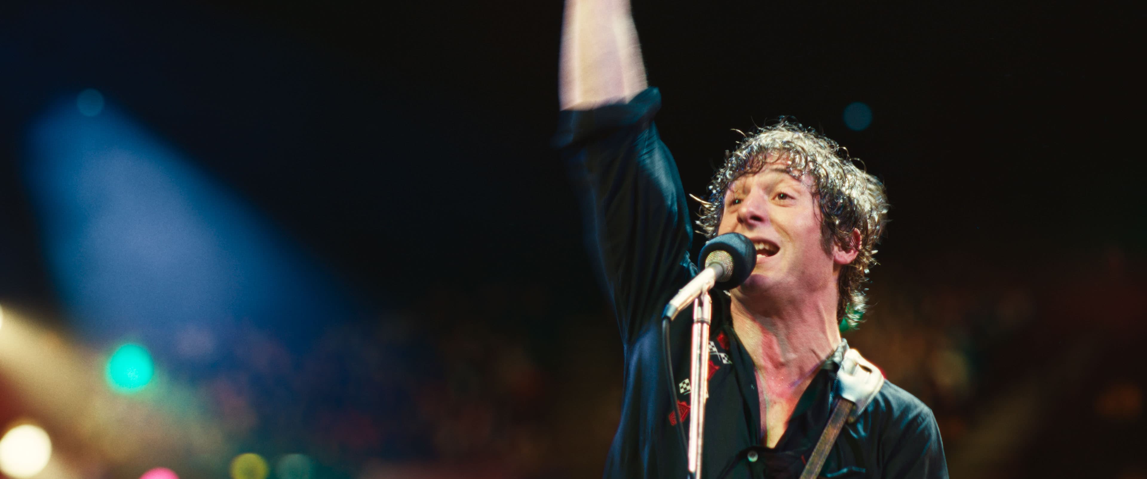 Actor Jeremy Allen White as Bruce Springsteen, singing on stage and playing a guitar in a still from "Deliver Me From Nowhere." 