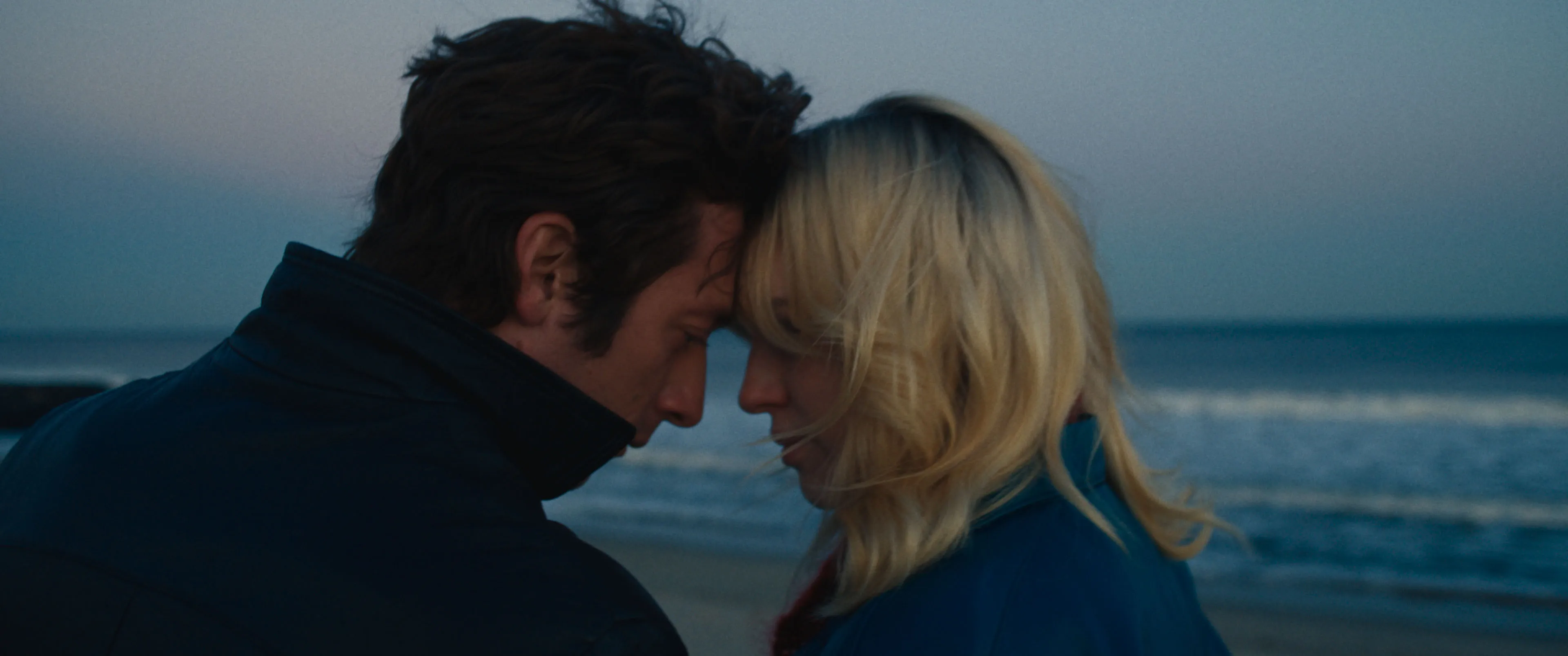 Actors Jeremy Allen White and Odessa Young lean in towards each other on a beach  in a still from "Deliver Me From Nowhere." 