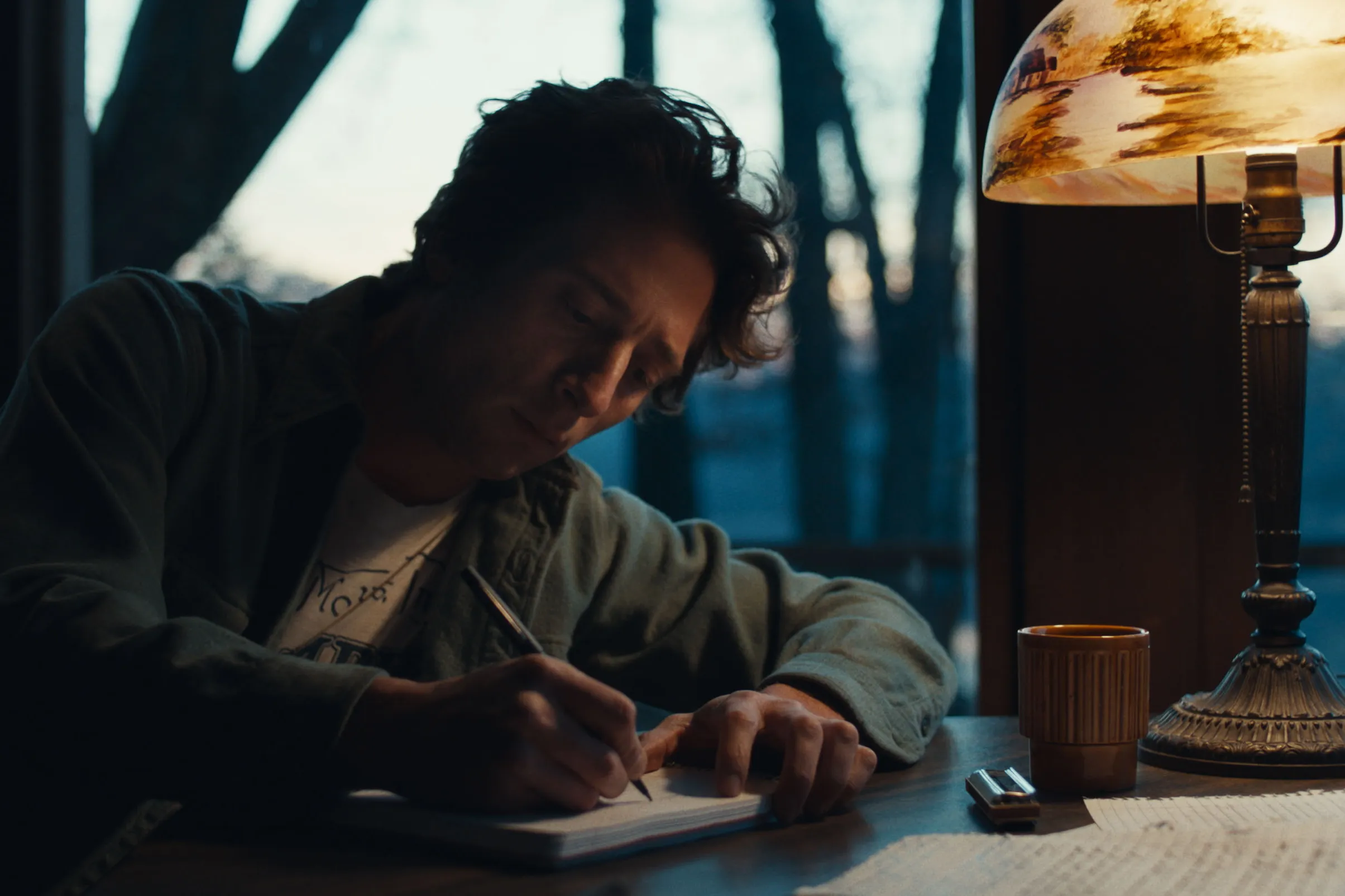 Actor Jeremy Allen White as Bruce Springsteen, writes in a notebook in a still from "Deliver Me From Nowhere." 