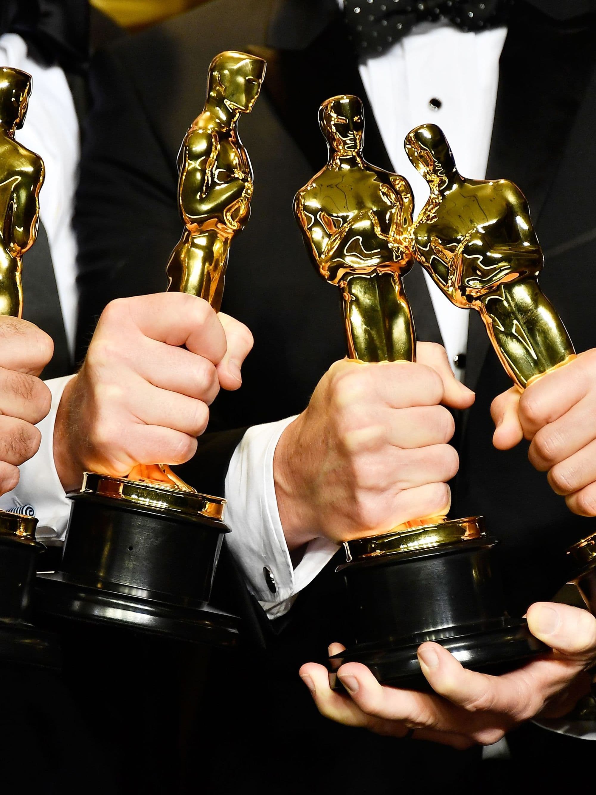 Hands holding four Oscar statuettes