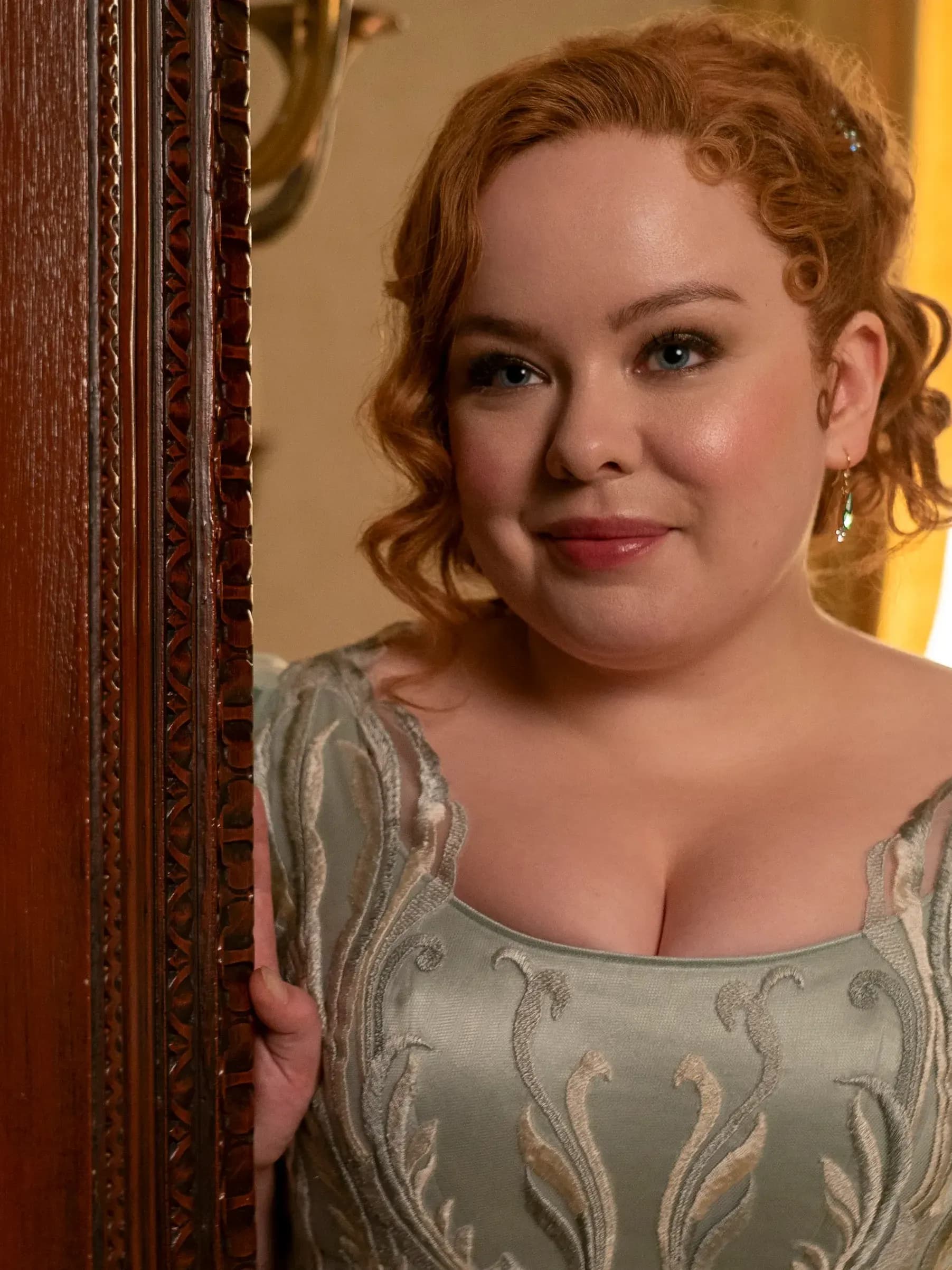 Nicola Coughlan stands at a doorway wearing a sparkling, seafoam-green dress in a scene from Bridgerton.