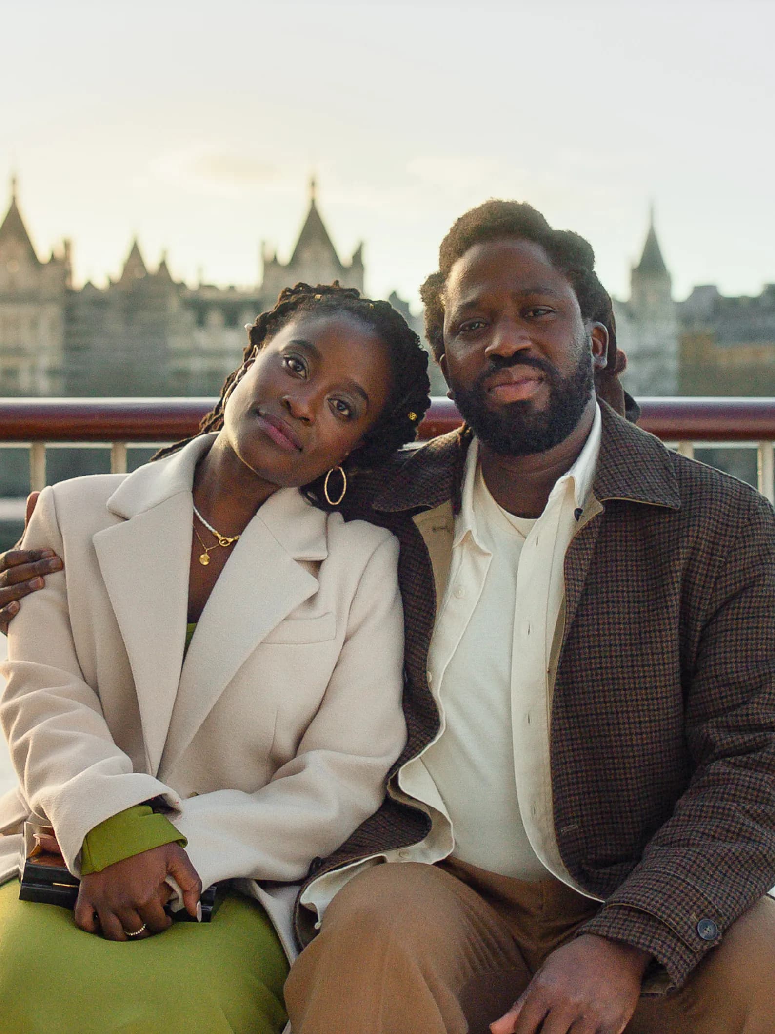 Actors Adjani Salmon and Babirye Bukilwa sit on a bench in front of the Thames River in a still from "Dreaming Whilst Black."