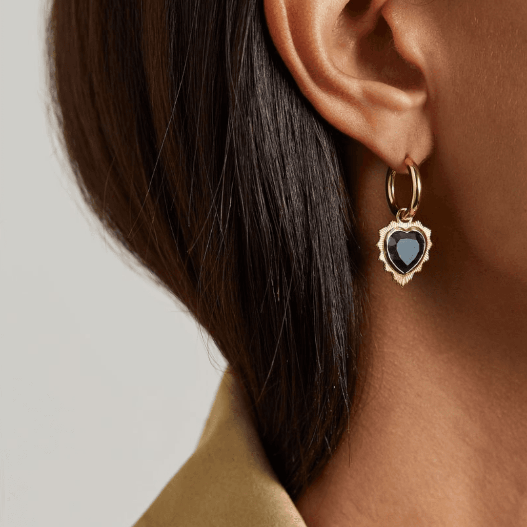 A close-up of a model's ear wearing the Foundrae Gemstone Heart 18-karat gold topaz single hoop earring