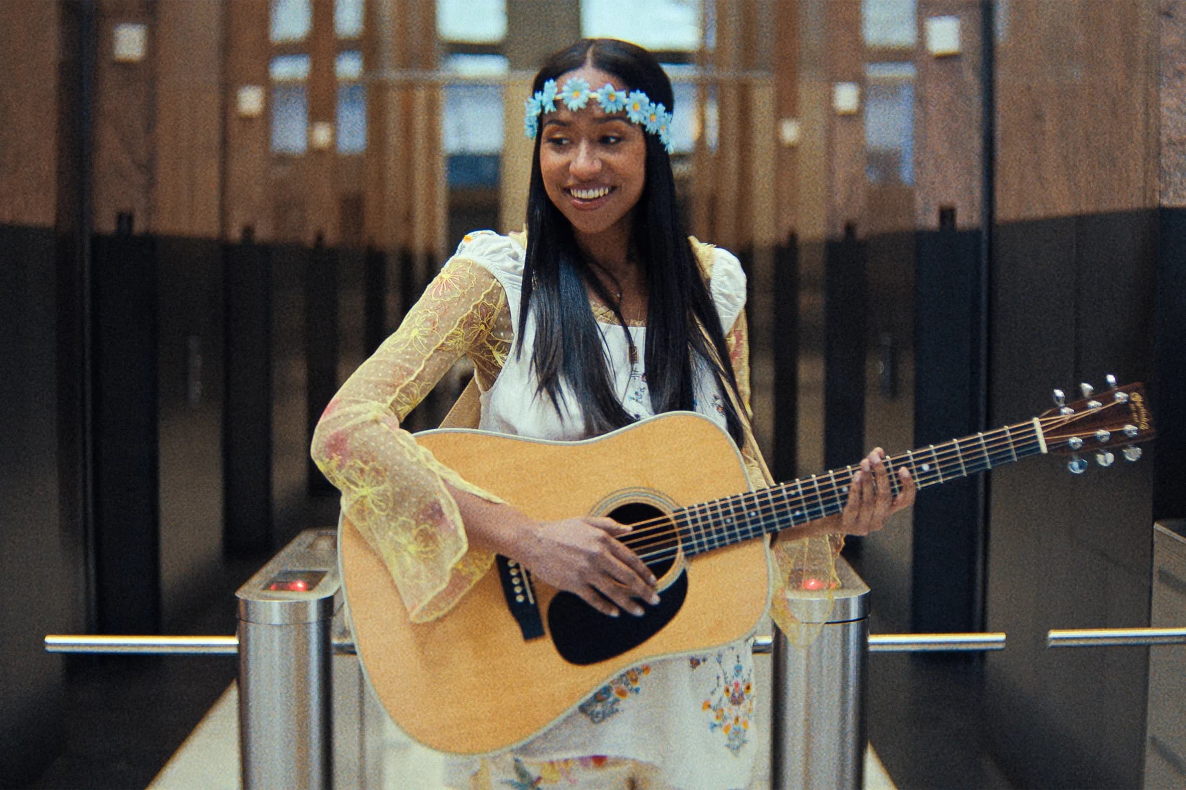 Actor Jensen Mcrae wears a flower crown and plays the guitar in a still from the film "Highest 2 Lowest.'