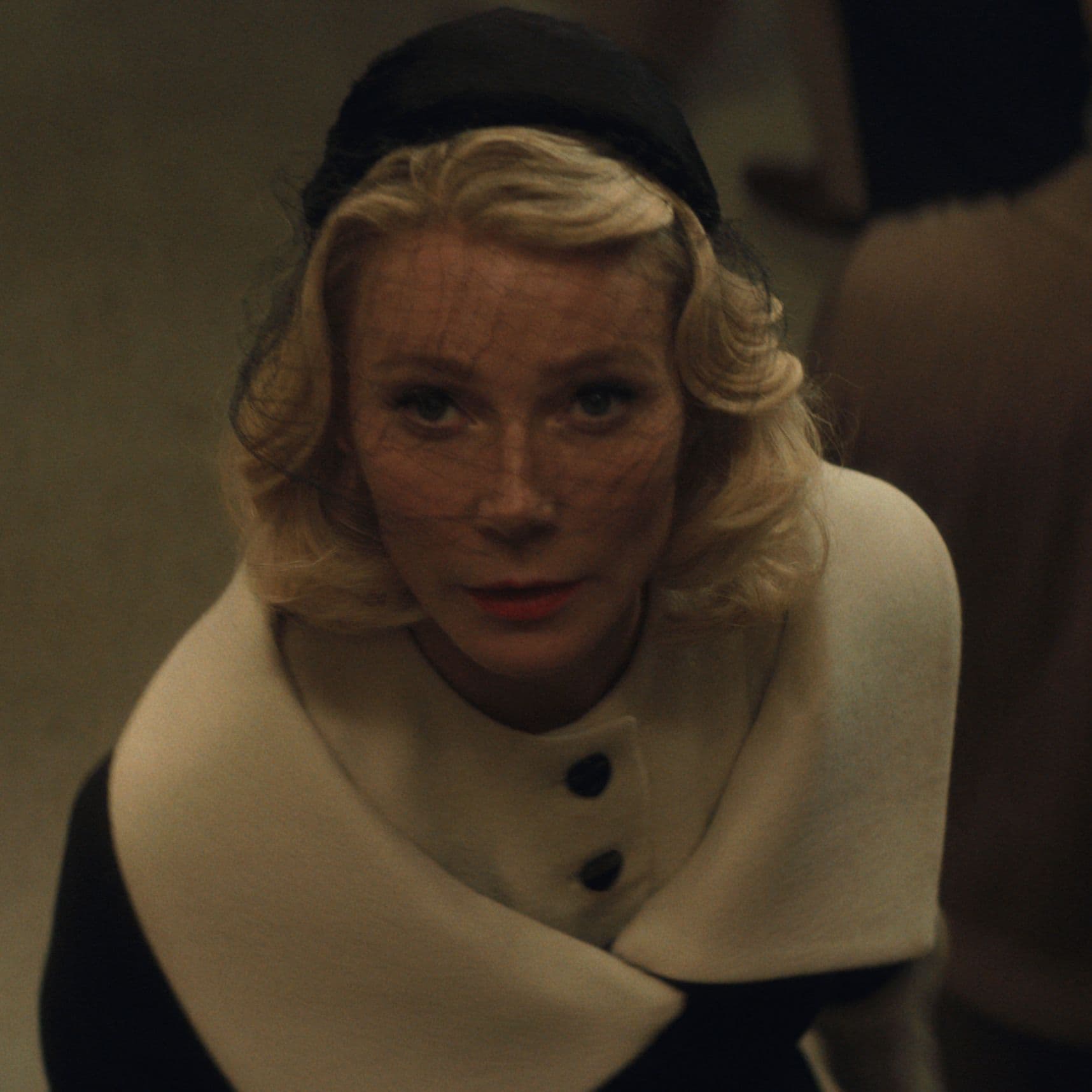 Gwyneth Paltrow in 50s-stule clothing, looking up at the camera in a scene from Marty Supreme.