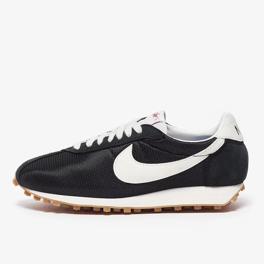 A pair of black Nike shoes with the white swoosh logo against an off-white background