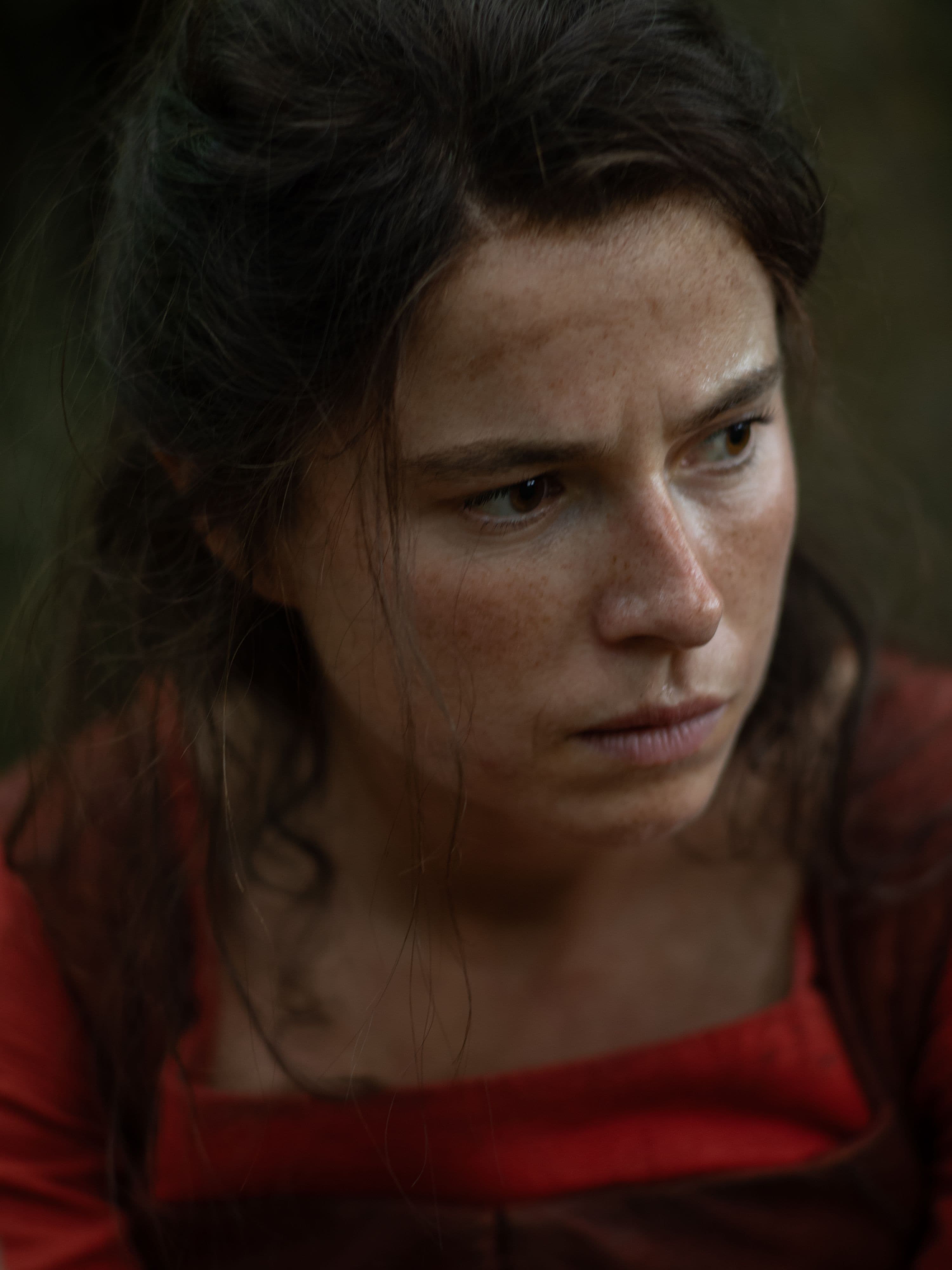 A close up of shot of actress Jesse Buckley wearing a red dress in a still from "Hamnet."